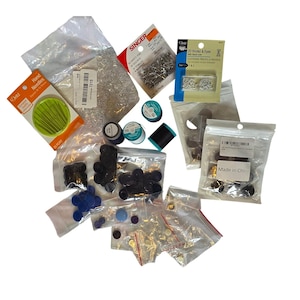 Könnte beinhalten: Eine Auswahl an Nähzubehör, darunter Nadeln, Sicherheitsnadeln, Haken und Ösen, Garnrollen und verschiedene Knöpfe in transparenten Plastiktüten. Das Bild zeigt auch eine Packung Dritz-Handnadeln.