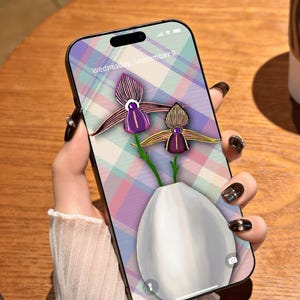 Könnte beinhalten: Ein Smartphone mit einer Hülle mit floralem Design. Die Hülle hat einen pastellfarbenen Karohintergrund und eine digitale Illustration von zwei Orchideen in einer weißen Vase. Der Bildschirm zeigt "Wednesday, September 9."