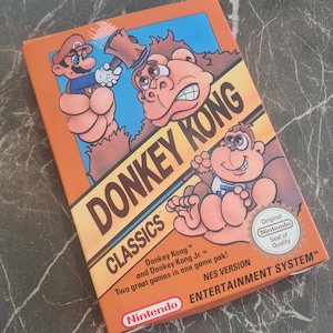 May include: A rectangular Donkey Kong Classics video game box for the Nintendo Entertainment System. The orange packaging features illustrations of Mario and Donkey Kong, the text Donkey Kong Classics, and an official Nintendo Seal of Quality.
