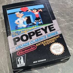 May include: A rectangular Nintendo Entertainment System video game box for The Original Popeye Arcade Classics Series. The black box features pixelated character art, the Nintendo logo, and the circular Original Nintendo Seal of Quality.