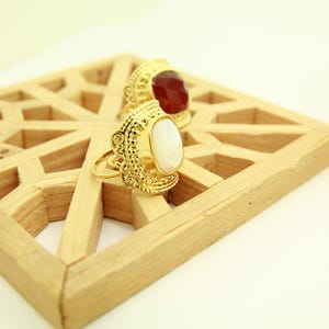 Peut inclure: Deux bagues en or avec des motifs ornés. Une bague a une pierre ovale blanche, et l'autre a une pierre ovale rouge.