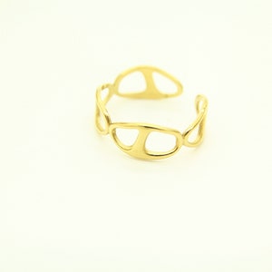 May include: A gold-toned ring with an abstract, openwork design. The ring is made of a series of connected, oval-shaped pieces.