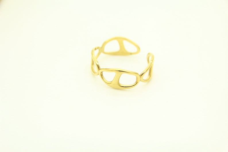 May include: A gold-toned ring with an abstract, openwork design. The ring is made of a series of connected, oval-shaped pieces.