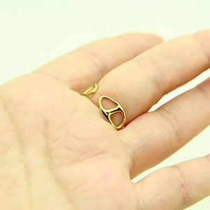 May include: A gold ring with a unique open design. The ring is worn on the middle finger of a hand.
