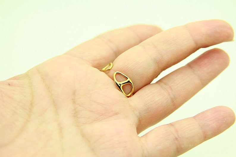 May include: A gold ring with a unique open design. The ring is worn on the middle finger of a hand.