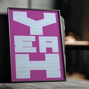 May include: Framed art print with the word "YEAH" in large, white, block letters against a vibrant magenta background. The artwork is displayed in a black frame and rests on a gray surface.
