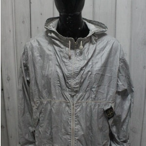 Może przedstawiać: Jasnoszara kurtka z kapturem i pełnym zapięciem na zamek błyskawiczny. Kurtka posiada sznurek w kapturze i w talii oraz małą naszywkę z logo na lewym rękawie. Kurtka jest prezentowana na manekinie.