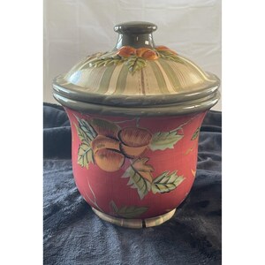 May include: A ceramic cookie jar with a lid. The jar is a deep red color with a painted design of acorns and leaves. The lid is light green with vertical stripes and a dark brown knob.