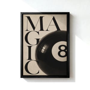以下が含まれることがあります： ベージュの背景に大きな黒いセリフ体のアルファベットで「MAGIC」と書かれた額装アートプリント。白い円形のインレイと数字の8が入った光沢のある黒いビリヤードのボールが、文字の上に配置されています。