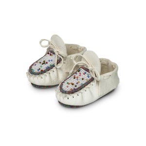 May include: A pair of off-white baby moccasins. The shoes feature a beaded design in various colors on the top of the foot. The moccasins have laces and are made of a soft, textured material. The soles are white with a stitched edge.