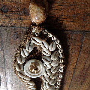 Könnte beinhalten: Eine braune und weiße Muschelkette mit einem großen Muschel Anhänger. Die Kette ist aus gewebtem Stoff und mit kleinen weißen Muscheln verziert.