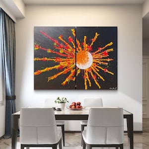 Pode incluir: Uma pintura em tela de duas peças apresentando um centro texturizado em forma de sol em branco e laranja, cercado por faixas radiantes de tinta amarela brilhante, laranja e vermelha contra um fundo preto sólido, exibido como arte de parede.