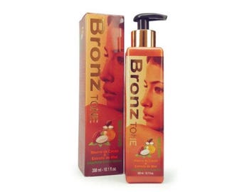 May include: A 300 ml bottle of Bronz Tone lotion with a matching rectangular box. The packaging is orange and brown, featuring a portrait of a person, the text Bronz Tone, and illustrations of cocoa butter and honey. The bottle has a black pump.