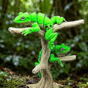 May include: A whimsical sculpture of two bright green frogs perched on a miniature tree branch. The frogs are segmented, giving them a unique appearance. The tree has a textured, light brown trunk and branches, set against a blurred green background.