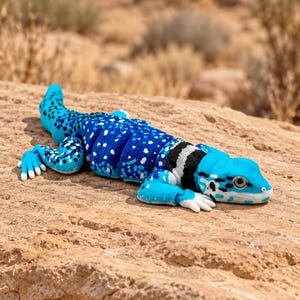 May include: A bright blue articulated lizard figurine with white spots, black markings, and white claws. The lizard features a segmented body design with a distinct black and white band around its neck and a textured surface finish.