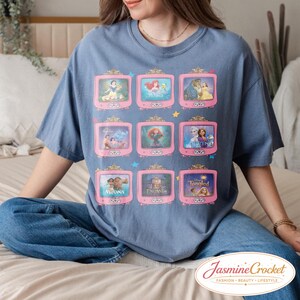 Op de afbeelding: Een blauw T-shirt met roze televisies met sc&egrave;nes uit animatiefilms. Het shirt heeft een ronde hals en korte mouwen. In de rechter benedenhoek van het shirt staat de tekst "Jasmine Crocket" in cursief.