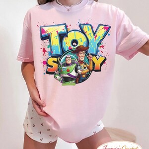 Puede incluir: Camiseta rosa claro con la inscripci&oacute;n "TOY STORY" en un estilo graffiti colorido. El dise&ntilde;o incluye a Buzz Lightyear y Woody. La camiseta de manga corta tiene un corte holgado, ideal para un look casual.