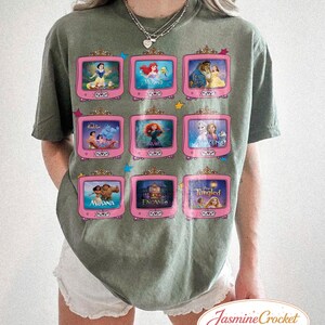 Op de afbeelding: Olijfgroen T-shirt met een ontwerp van negen roze televisies, elk met een sc&egrave;ne uit een animatiefilm. Het shirt heeft een ronde hals en korte mouwen. De tekst "Jasmine Crocket" staat rechtsonder.
