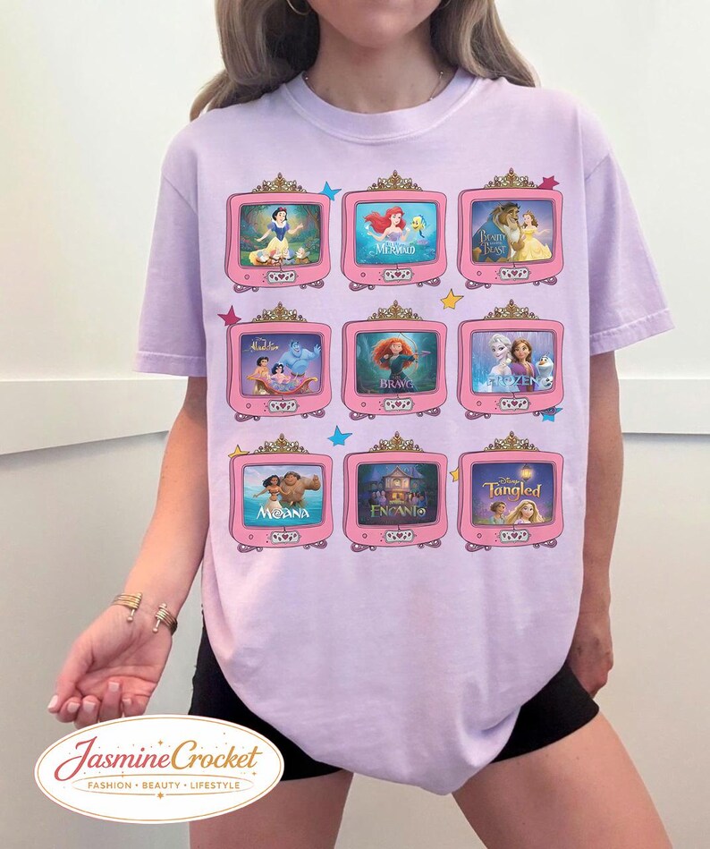 Op de afbeelding: Lichtpaars T-shirt met een raster van roze televisies, elk met een sc&egrave;ne uit een animatiefilm. De top heeft een ronde hals en korte mouwen. De tekst "Jasmine Crocket" staat onderaan.