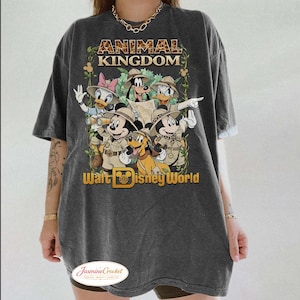 Op de afbeelding: Donkergrijze t-shirt met een afbeelding van Disney-personages in safari-outfits, waaronder Mickey Mouse, Donald Duck en Goofy. De teksten "ANIMAL KINGDOM" en "Walt Disney World" staan boven en onder de personages.