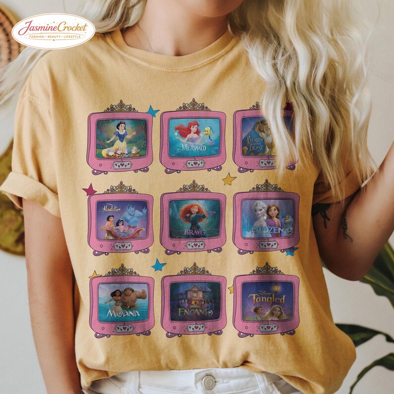 Op de afbeelding: Mosterdgeel T-shirt met een raster van roze televisies, elk met een andere animatiefilmsc&egrave;ne. Het shirt heeft de tekst "Jasmine Crochet" linksboven. De films zijn Sneeuwwitje, De Kleine Zeemeermin, Belle en het Beest, Aladdin, Merida, Frozen, Vaiana, Encanto en Rapunzel.