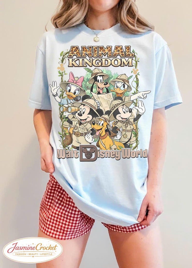 Op de afbeelding: Lichtblauw T-shirt met een afbeelding van Disney-personages in safari-outfits, met de tekst "ANIMAL KINGDOM" en "Walt Disney World". Het ontwerp bevat Mickey Mouse, Minnie Mouse, Donald Duck, Daisy Duck, Goofy en Pluto.