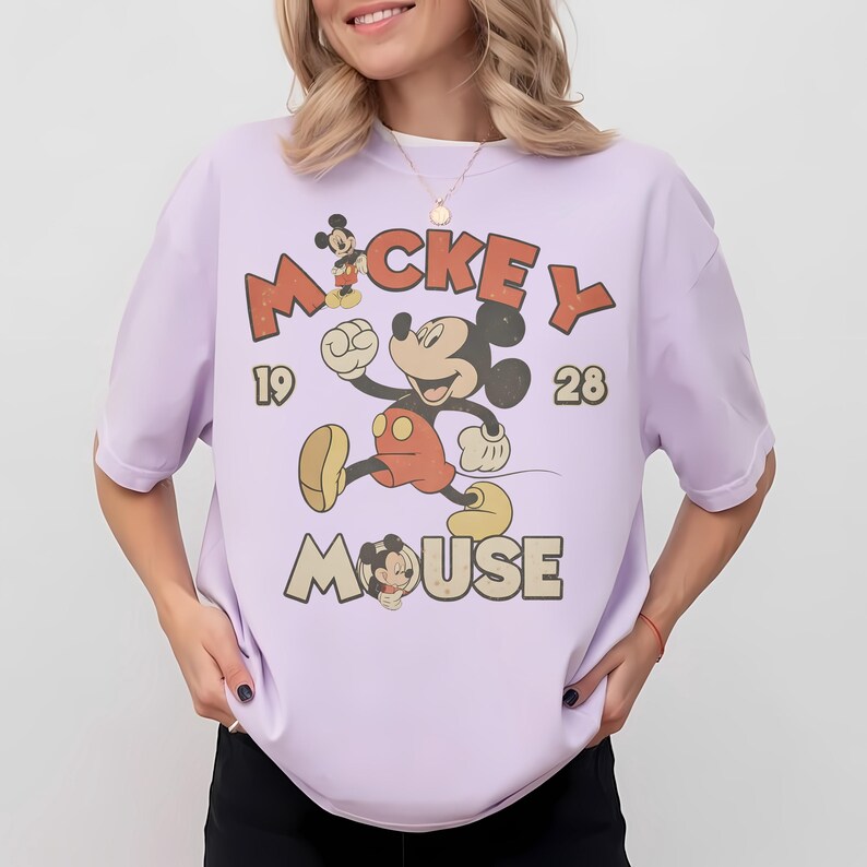 Op de afbeelding: Lichtpaars T-shirt met een vintage Mickey Mouse-ontwerp. De afbeelding toont Mickey Mouse die rent, met de woorden "Mickey Mouse" en de cijfers "1928". Het shirt heeft korte mouwen.