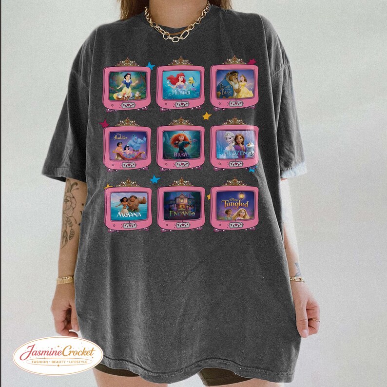 Op de afbeelding: Donkergrijs T-shirt met negen roze televisieschermen, elk met een sc&egrave;ne uit een animatiefilm. De schermen zijn gerangschikt in een raster, met sterren en een kroonontwerp. Het T-shirt heeft een losse pasvorm.