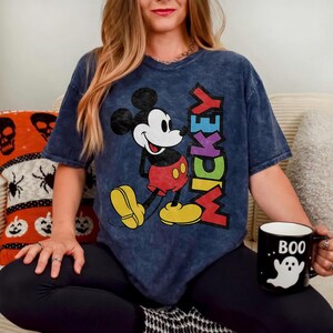May include: Navy blue t-shirt featuring Mickey Mouse with the word "Mickey" in colourful letters. The shirt is paired with black leggings. A black mug with a white ghost and the word "BOO" is also visible.