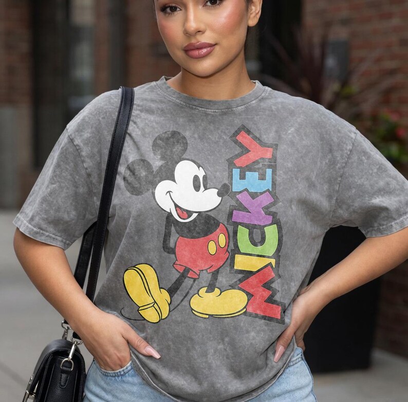 May include: Grey t-shirt with a Mickey Mouse graphic and the word "MICKEY" in rainbow colours. The cartoon character is wearing red shorts and yellow shoes. The shirt has a vintage, washed appearance.