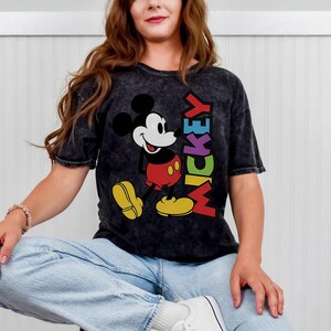 May include: Black t-shirt with a Mickey Mouse graphic. The design shows Mickey in red shorts and yellow shoes, with the word "MICKEY" in rainbow colours. The tee has a vintage, washed appearance.