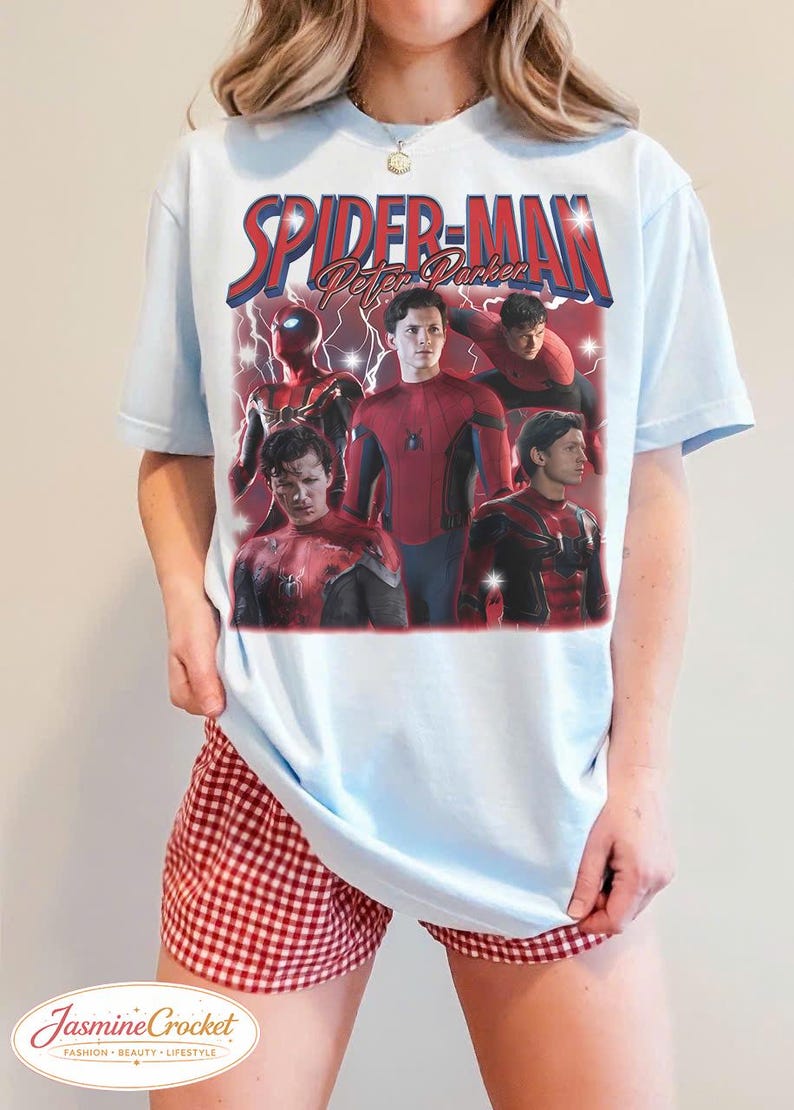 以下が含まれることがあります： 水色のTシャツ。赤と青で「Spider-Man Peter Parker」の文字とスパイダーマンのグラフィックがプリントされています。スパイダーマンの複数の画像が含まれています。モデルは赤と白のチェック柄のショートパンツを着用しています。