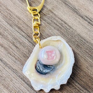 牡蠣の殻のキーホルダーチャーム。粘土製のモノグラム「パール」の文字と色をカスタマイズ可能。
