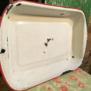 May include: White enamel baking dish with a red rim. The dish has some black marks and scratches on the surface.