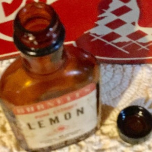 May include: A brown glass bottle with a clear glass stopper. The bottle is labeled "Schnapps Lemon" in white lettering on a red background.