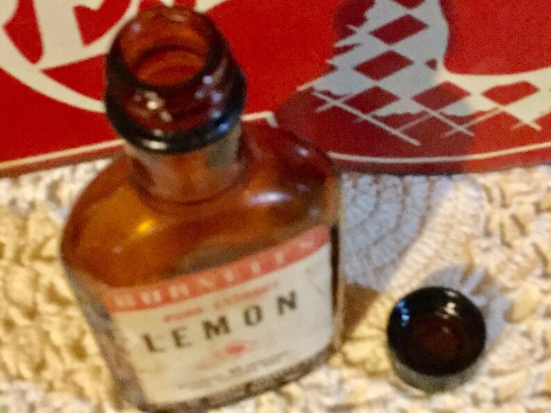 May include: A brown glass bottle with a clear glass stopper. The bottle is labeled "Schnapps Lemon" in white lettering on a red background.