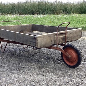 May include: A red metal wagon with a wooden box. The box is made of weathered wood and has the words 