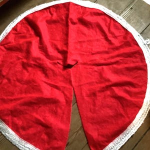 May include: A round, red Christmas tree skirt with a white, sequined trim. The skirt is made of a soft, possibly satin-like material. The skirt has a slit to wrap around the tree trunk.