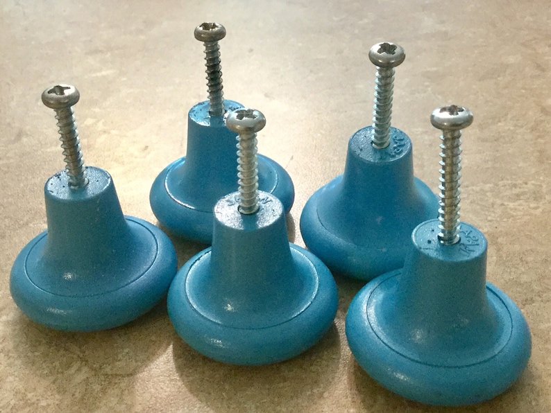 K&ouml;nnte beinhalten: F&uuml;nf blaue Kunststoff-Schrankkn&ouml;pfe mit silbernen Schrauben. Die Kn&ouml;pfe sind rund mit einem erh&ouml;hten Rand und einer leicht vertieften Mitte.