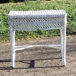 May include: A white wicker side table with a rectangular top and four legs. The table has a woven design on the top and sides, and measures approximately 24 inches tall.