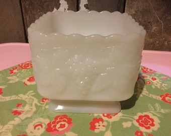 May include: White milk glass square bowl with a scalloped rim and a raised floral design. The bowl has a square base.