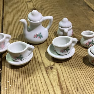 May include: A miniature tea set with a white teapot, creamer, sugar bowl, and two teacups and saucers. The set is decorated with pink flowers and green leaves.