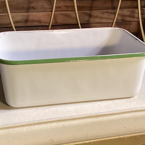 May include: A rectangular enamel baking pan with a smooth white finish and a thin green rim around the top edge. The interior of the pan is white, and the exterior features rounded corners with a clean, glossy surface throughout the entire piece.