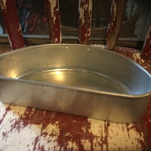May include: A silver half-circle baking pan with a smooth, shiny surface. The pan has a slightly rounded bottom and a straight rim. It is sitting on a wooden surface.