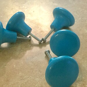 K&ouml;nnte beinhalten: F&uuml;nf blaue Holzkn&ouml;pfe mit silbernen Schrauben. Die Kn&ouml;pfe sind rund und haben eine leichte Vertiefung in der Mitte.