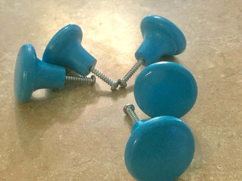 K&ouml;nnte beinhalten: F&uuml;nf blaue Holzkn&ouml;pfe mit silbernen Schrauben. Die Kn&ouml;pfe sind rund und haben eine leichte Vertiefung in der Mitte.