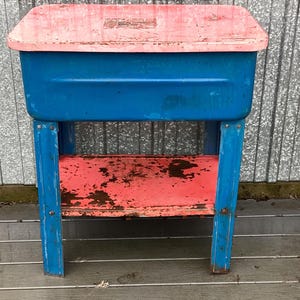 May include: A vintage metal parts washing station with a blue tub and a red top. The station has a shelf underneath for storage.