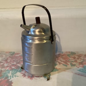 May include: A silver aluminum coffee pot with a black handle and a brown lid. The pot has a measurement scale on the side.