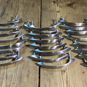 May include: A set of 18 silver-toned cabinet drawer pulls with a curved, modern design. The pulls are arranged in three rows of six.