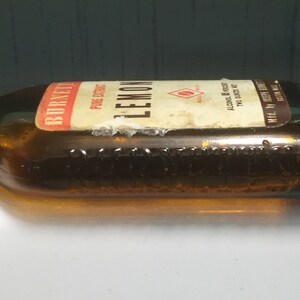 May include: A brown glass bottle with a label that reads "Burnett's Lemon Pure Extract" and "Alcohol 6% by Volume 70% Alcohol by Weight".